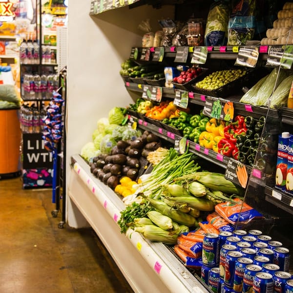A grocery store aisle filled with colorful fresh produce, fruits, and packaged beverages.