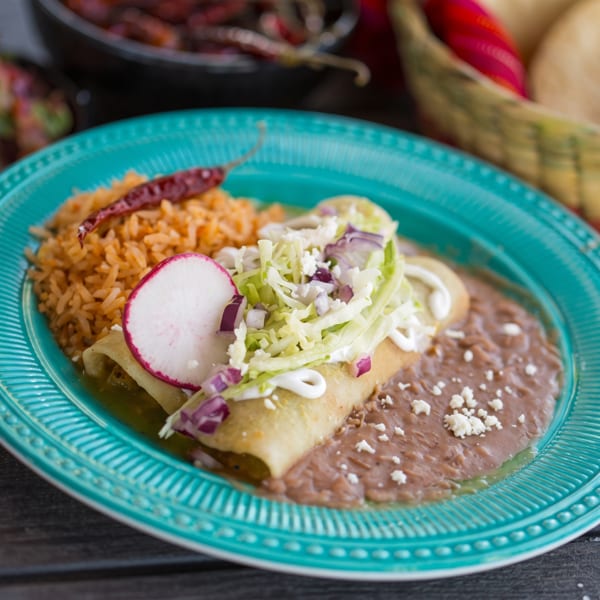 Mexican enchilada with rice, beans, radish, lettuce, and sour cream on a turquoise plate.