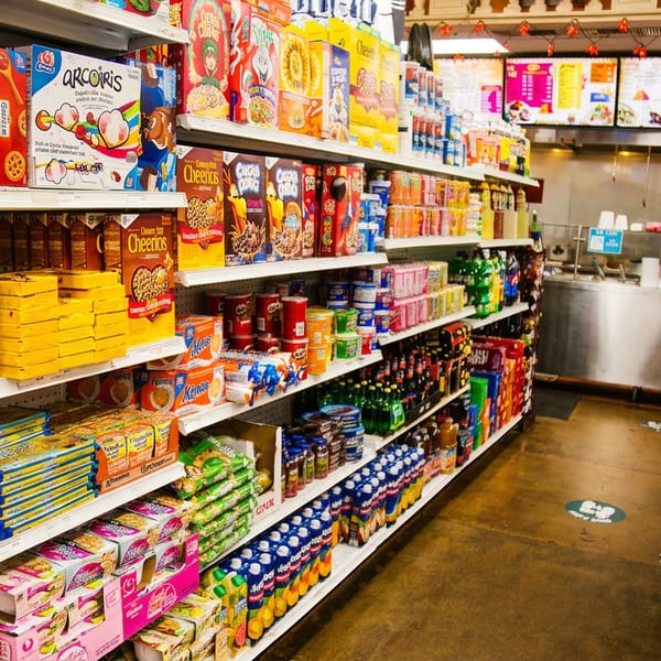 Store aisle with shelves of packaged food and a restaurant counter with menus in the background.