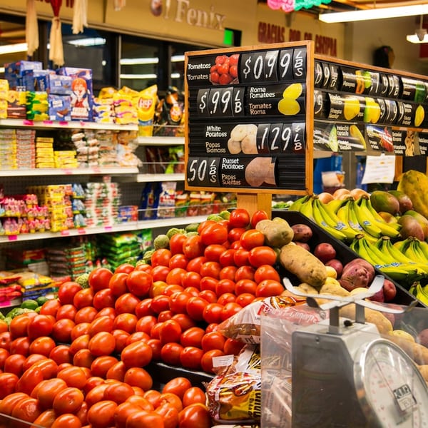 Fresh produce display with piles of tomatoes, bananas, papayas, and potatoes in a grocery store.